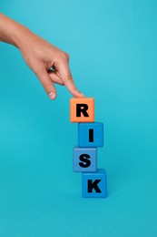 Woman making word Risk with colorful cubes on turquoise background, closeup