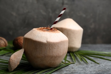 Young peeled coconut with straw and palm leaf on grey table