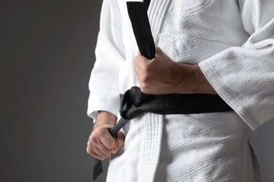 Karate coach wearing kimono and black belt on grey background, closeup. Space for text