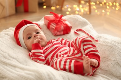 Cute little baby wearing Santa hat on blanket in room with Christmas lights