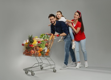 Happy family with shopping cart full of groceries on grey background