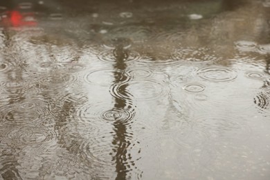 Rain drops falling down onto puddle outdoors