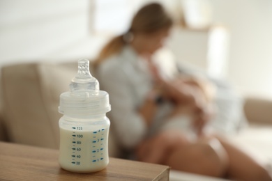 Mother breastfeeding her little baby at home, focus on bottle with milk. Healthy growth