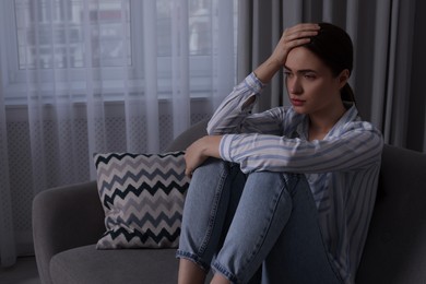 Unhappy young woman on sofa at home, space for text. Loneliness concept