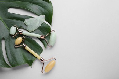 Photo of Gua sha stone, different face rollers and monstera leaf on light background, flat lay. Space for text