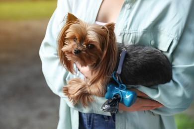 Photo of Woman holding her cute dog with waste bags in park, closeup