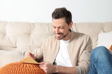 Photo of Happy man writing message in greeting card in living room