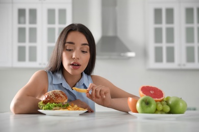 Photo of Concept of choice between healthy and junk food. Woman eating French fries in kitchen