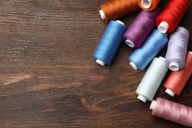 Photo of Different colorful sewing threads on wooden table, flat lay. Space for text