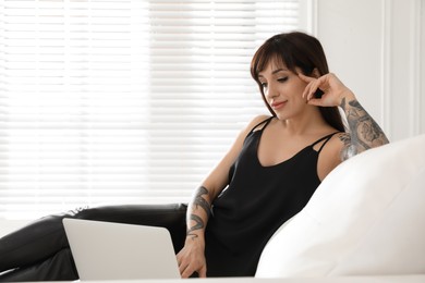Beautiful woman with tattoos on arms using laptop in living room