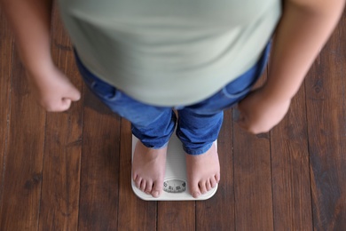 Overweight boy standing on floor scales indoors, above view