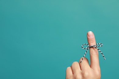 Photo of Woman showing index finger with tied bow as reminder on light blue background, closeup. Space for text