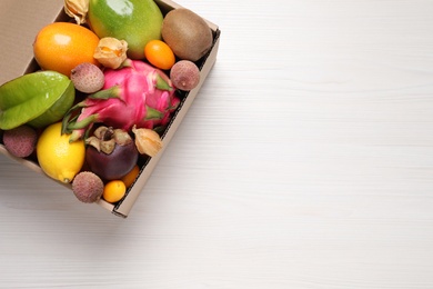Cardboard box with different exotic fruits on white wooden table, top view. Space for text