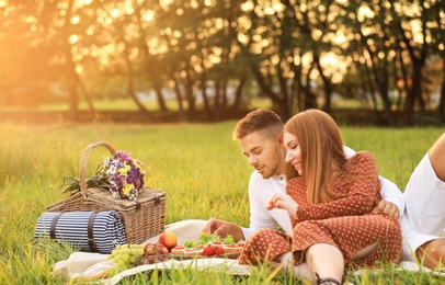 Photo of Happy young couple having picnic with tasty snacks in park