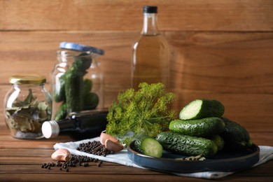 Photo of Fresh cucumbers and other ingredients near jars prepared for canning on wooden table. Space for text