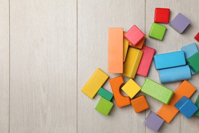 Colorful building blocks on wooden floor, flat lay. Space for text