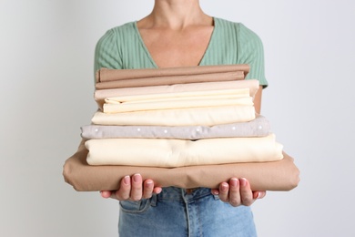 Woman holding stack of clean bed linens on light grey background
