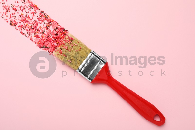 Brush painting with red sprinkles on pink background, top view. Creative concept