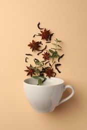 Photo of Anise stars, dry tea and mint falling into cup on beige background, flat lay