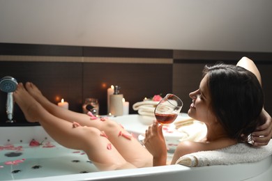 Woman holding glass of wine while taking bath with rose petals. Romantic atmosphere