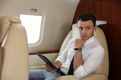 Businessman with earbuds working on tablet in airplane during flight