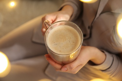 Woman holding cup with hot drink indoors, closeup