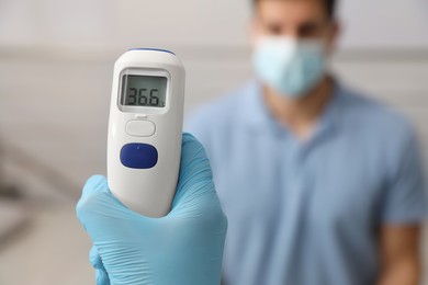 Doctor measuring man's temperature indoors, closeup. Prevent spreading of Covid-19