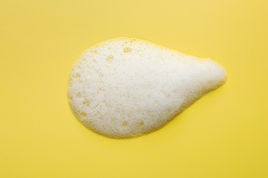 Drop of fluffy soap foam on yellow background, top view