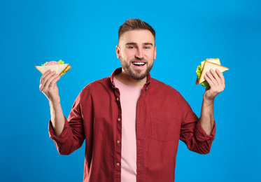 Photo of Young man with tasty sandwiches on light blue background