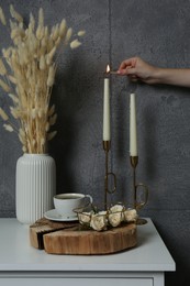 Woman lighting candle on table near grey wall indoors, closeup. Interior design