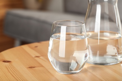 Jug and glass of water on wooden table in room, closeup with space for text. Refreshing drink