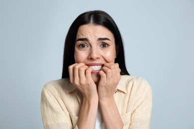 Scared young woman biting her nails on light grey background