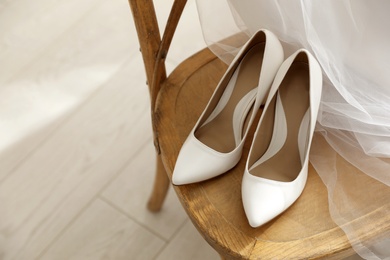 Pair of white wedding high heel shoes and veil on wooden chair indoors