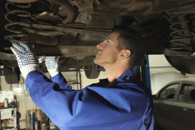 Professional mechanic fixing lifted car at automobile repair shop