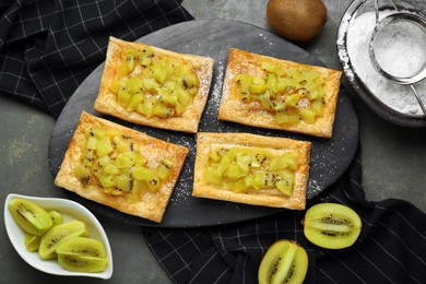 Photo of Fresh tasty puff pastry with sugar powder and kiwi served on grey table, flat lay
