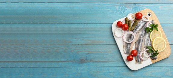 Image of Serving board with salted herring fillets, parsley, onion rings, pickles, cherry tomatoes and lemon on light blue wooden table, top view with space for text. Banner design
