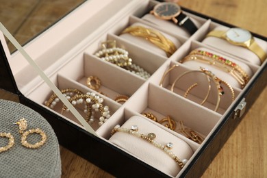 Elegant jewelry box with beautiful bijouterie and expensive wristwatches on wooden table, closeup