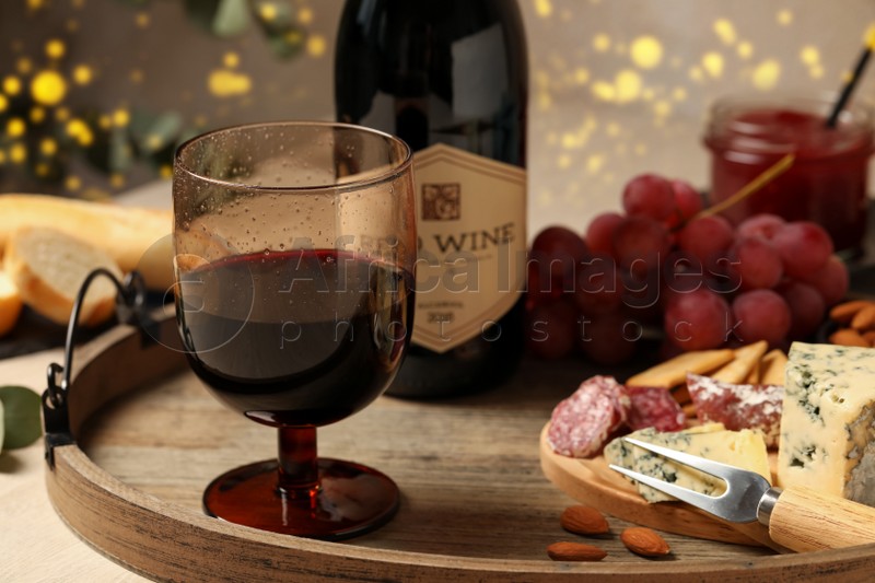 Glass of tasty red wine near bottle and delicious snacks on wooden table