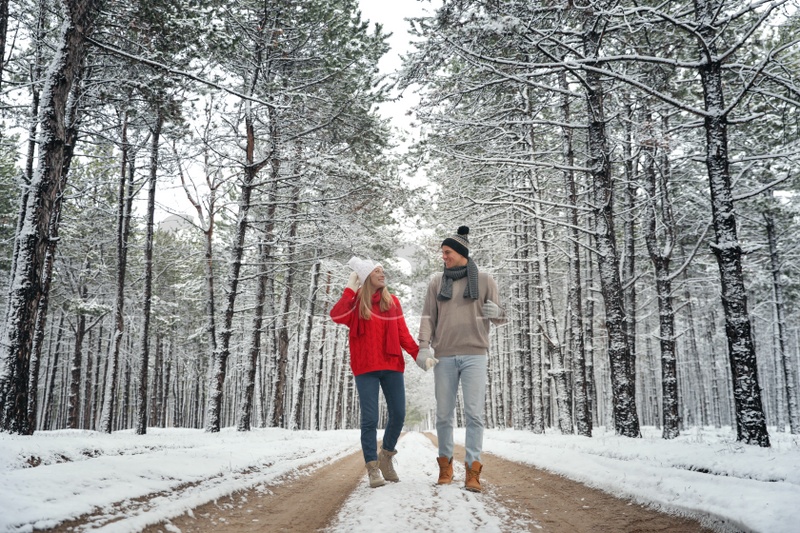 Beautiful happy couple walking through snowy forest on winter day