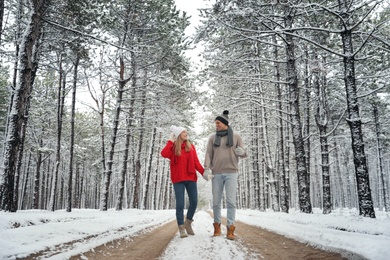 Beautiful happy couple walking through snowy forest on winter day