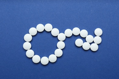 Male sign with bent arrow of white pills symbolizing potency problems on blue background, flat lay