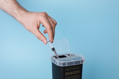 Man throwing used syringe into sharps container on light blue background, closeup