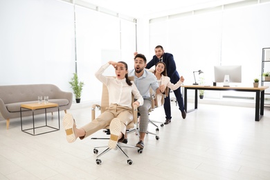 Happy office employees riding chairs at workplace