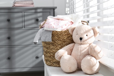 Wicker laundry basket with different clothes and teddy bear on window sill indoors. Space for text