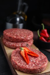 Raw hamburger patties with chili pepper on black table, closeup