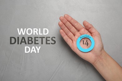 Woman holding blue paper circle as World Diabetes Day symbol at grey table, top view 