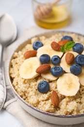 Photo of Bowl of delicious cooked quinoa with almonds, bananas and blueberries on white table, closeup