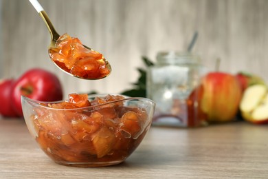 Spoon with tasty apple jam over glass bowl at wooden table, space for text