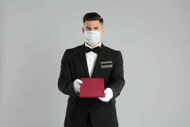 Waiter in medical face mask with menu on light grey background