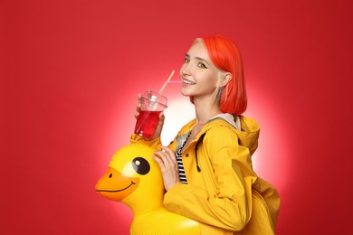 Beautiful young woman with bright dyed hair and inflatable ring drinking refreshing cocktail on color background